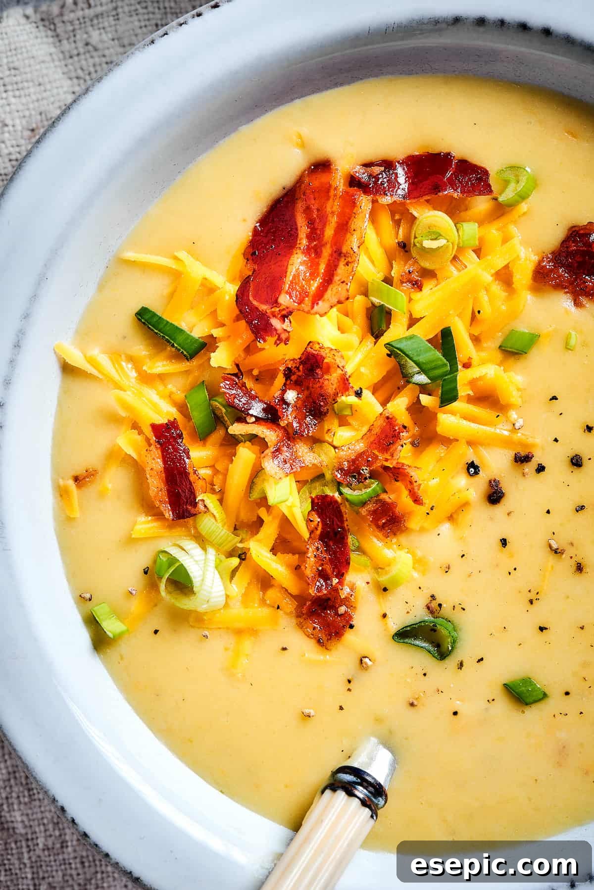 A close-up shot of a bowl of creamy baked potato soup, artfully garnished with crunchy bacon, fresh green onions, and melted cheese, ready for enjoyment.
