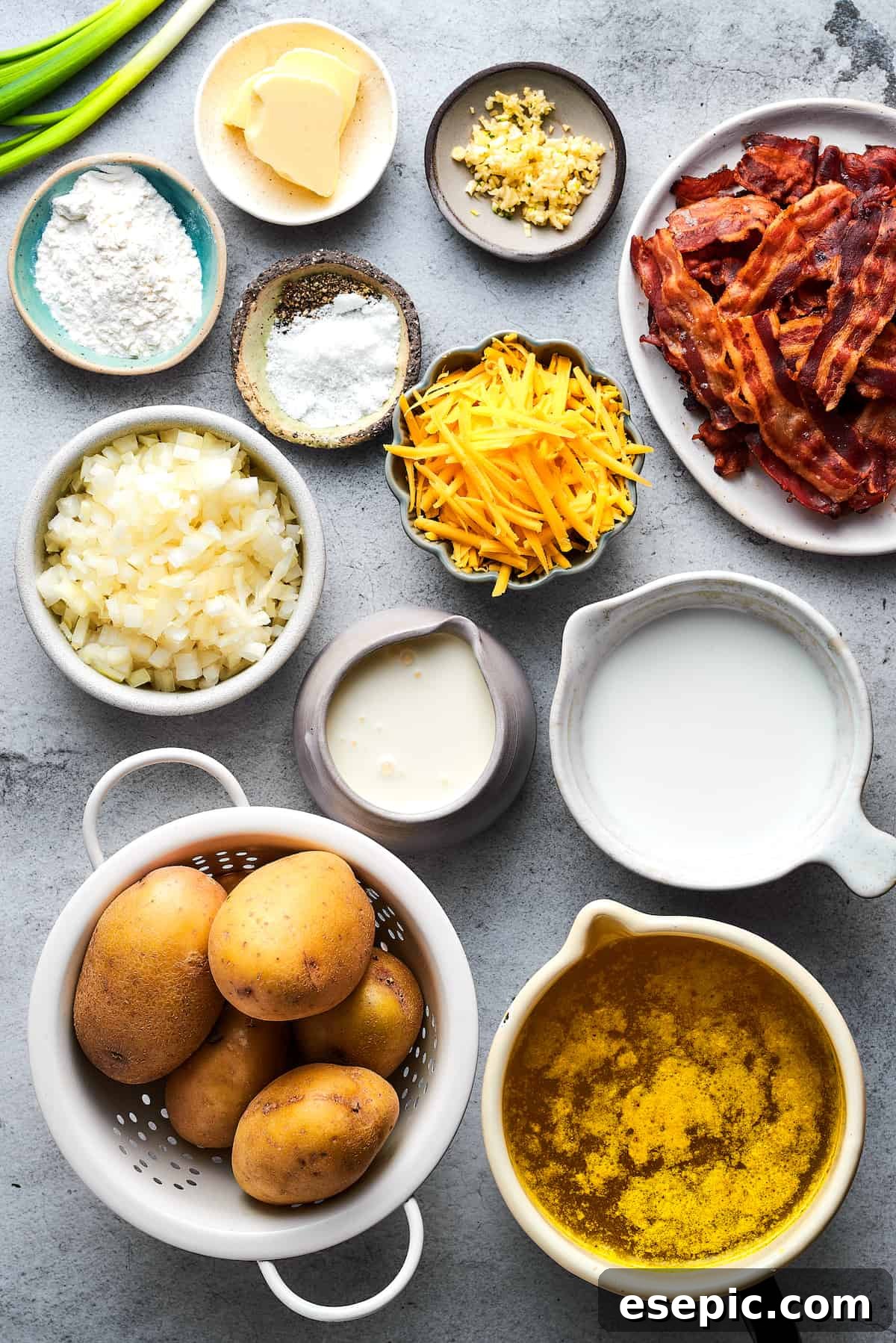 All the fresh ingredients for homemade baked potato soup laid out neatly on a rustic wooden work surface, including potatoes, cheese, butter, onions, garlic, and herbs.