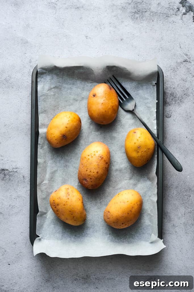 Four large potatoes, thoroughly washed and pricked with a fork, arranged on a baking sheet lined with parchment paper, ready for baking.