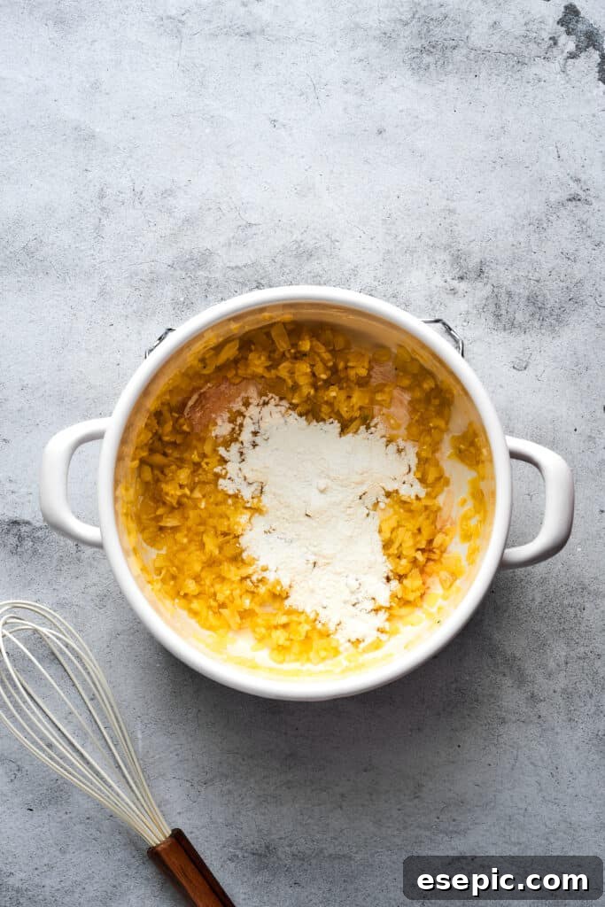 A small amount of all-purpose flour being sprinkled into a soup pot containing sautéed onions, melted butter, and fragrant garlic, forming the initial roux.