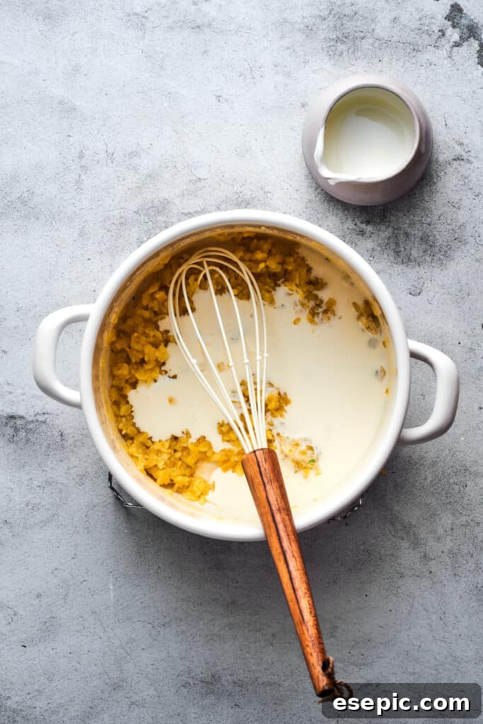 A whisk actively stirring milk into the soup pot, gently combining it with the roux and other ingredients to create a smooth, creamy base.