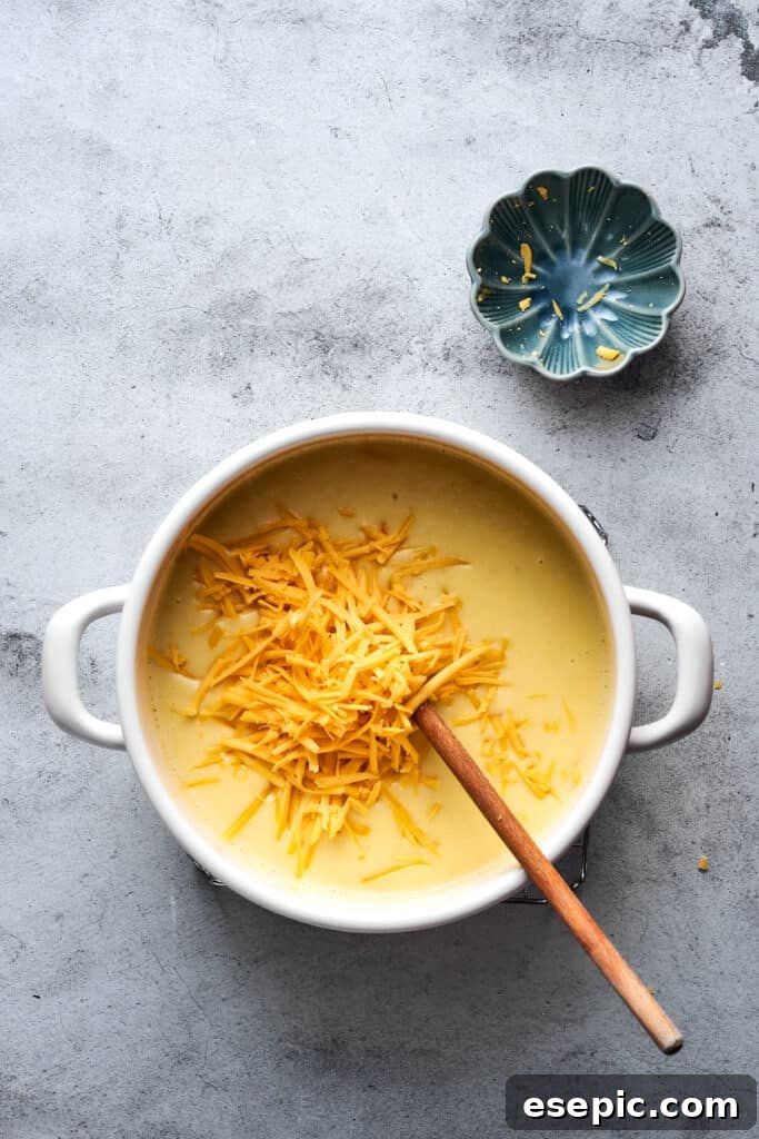 A generous amount of shredded cheddar cheese being added to a pot of hot, creamy potato soup, ready to be stirred until melted and smooth.