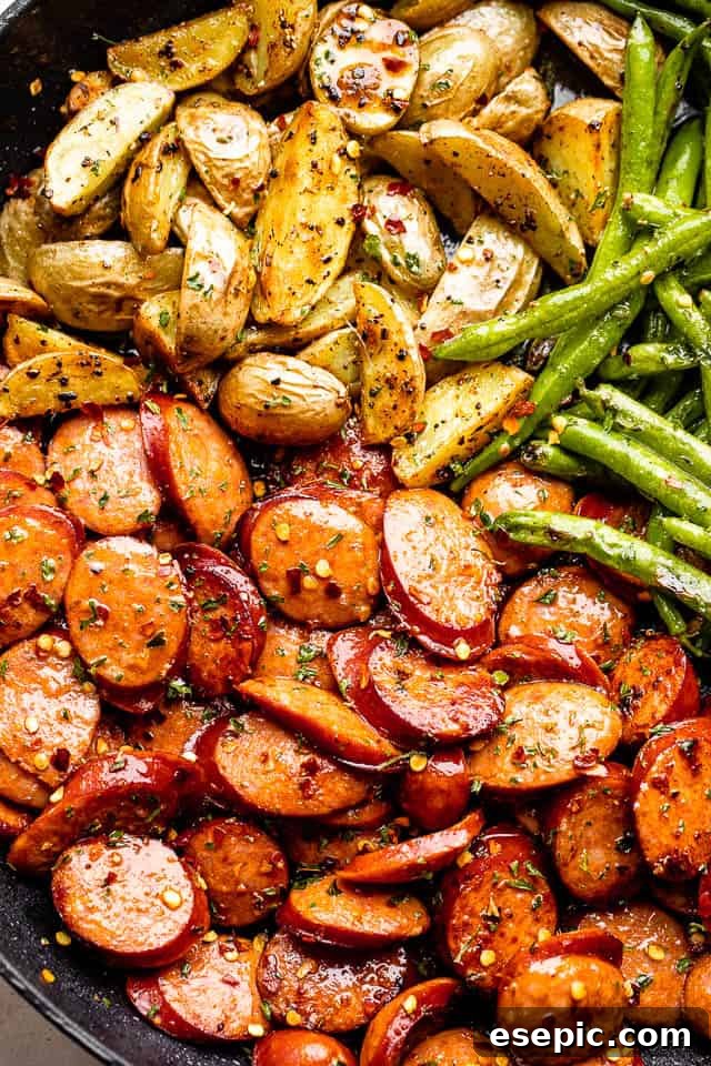 Close-up of golden-brown andouille sausage slices and quartered Yukon potatoes lightly seasoned with pepper flakes, sizzling in a hot skillet.