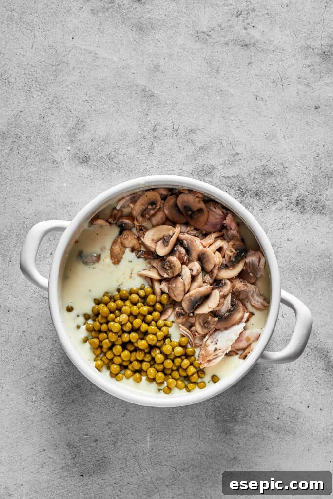 Mushrooms, cream, peas, and other ingredients being combined in a pot, creating the base for the tetrazzini casserole.