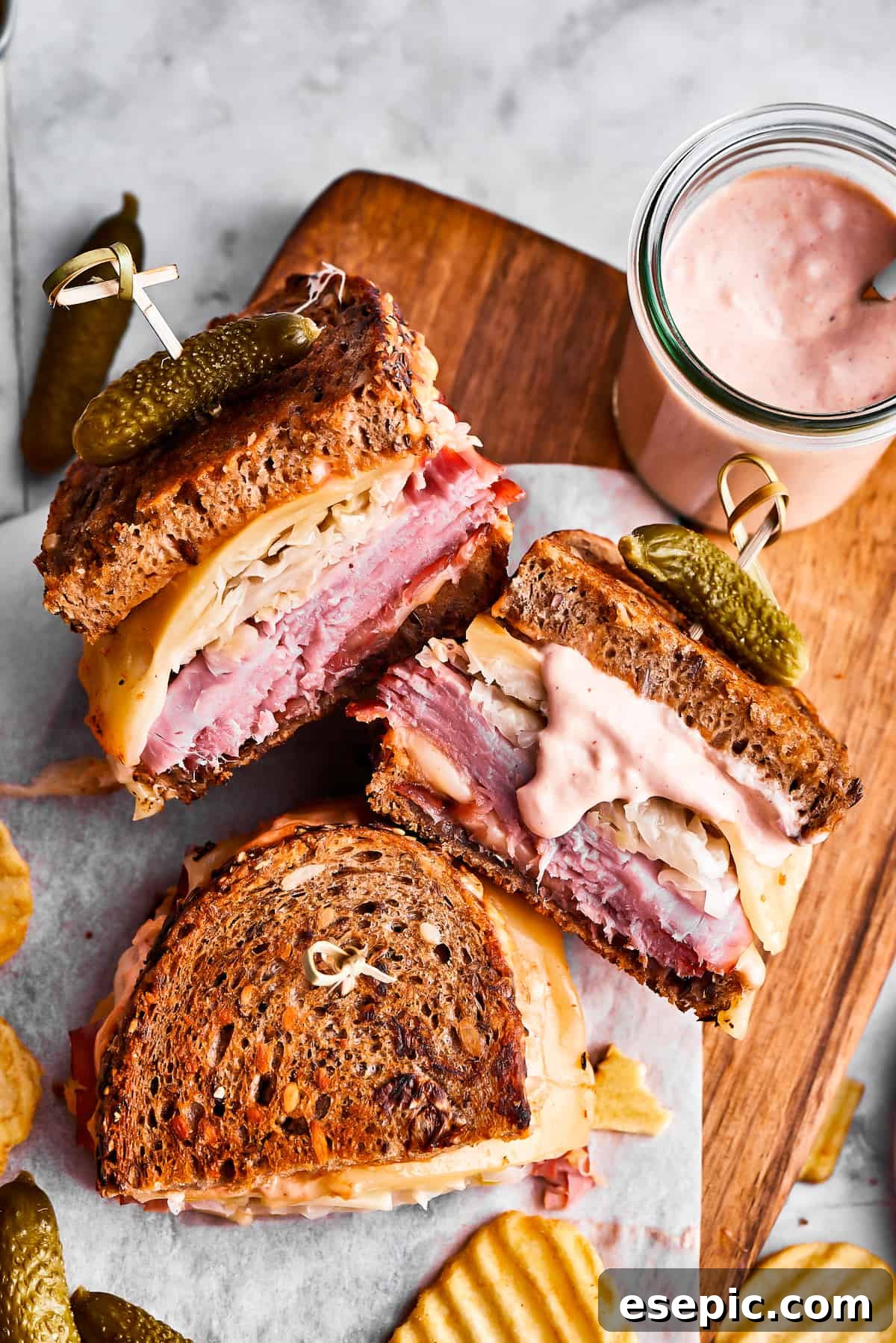 Three Reuben sandwich halves, some potato chips, and a jar of dressing on a cutting board.