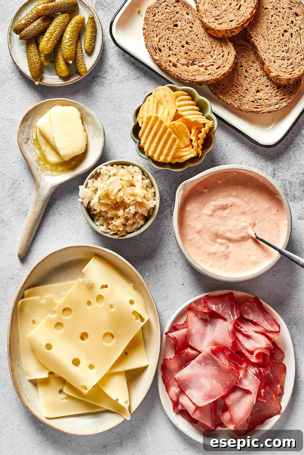 Pickles, bread, potato chips, russian dressing, sliced corned beef, swiss cheese, sauerkraut, and butter.