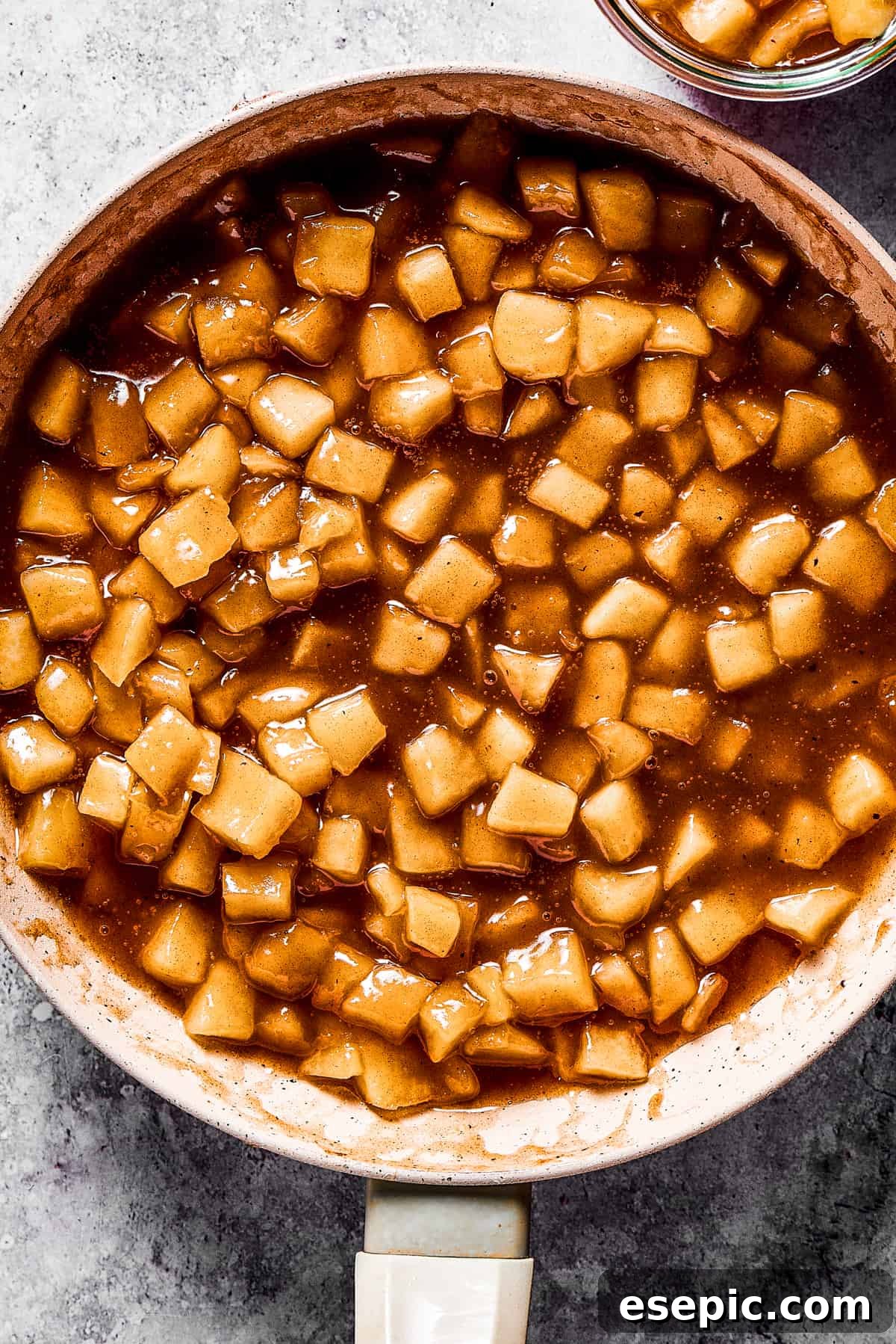 Making homemade apple pie filling in a skillet, showcasing the tender apple slices and rich, spiced syrup.