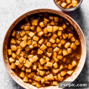 Homemade apple pie filling in a white skillet, and a small jar of the filling set right next to the skillet.