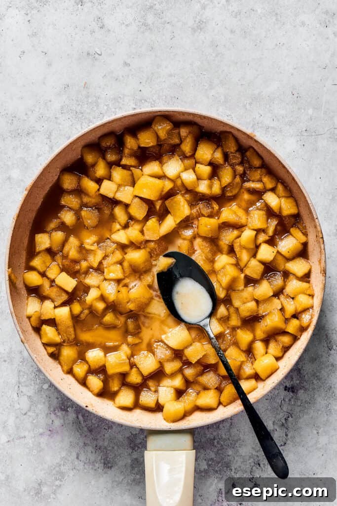 A small dish holding a smooth cornstarch slurry, prepared to thicken the simmering apple pie filling.