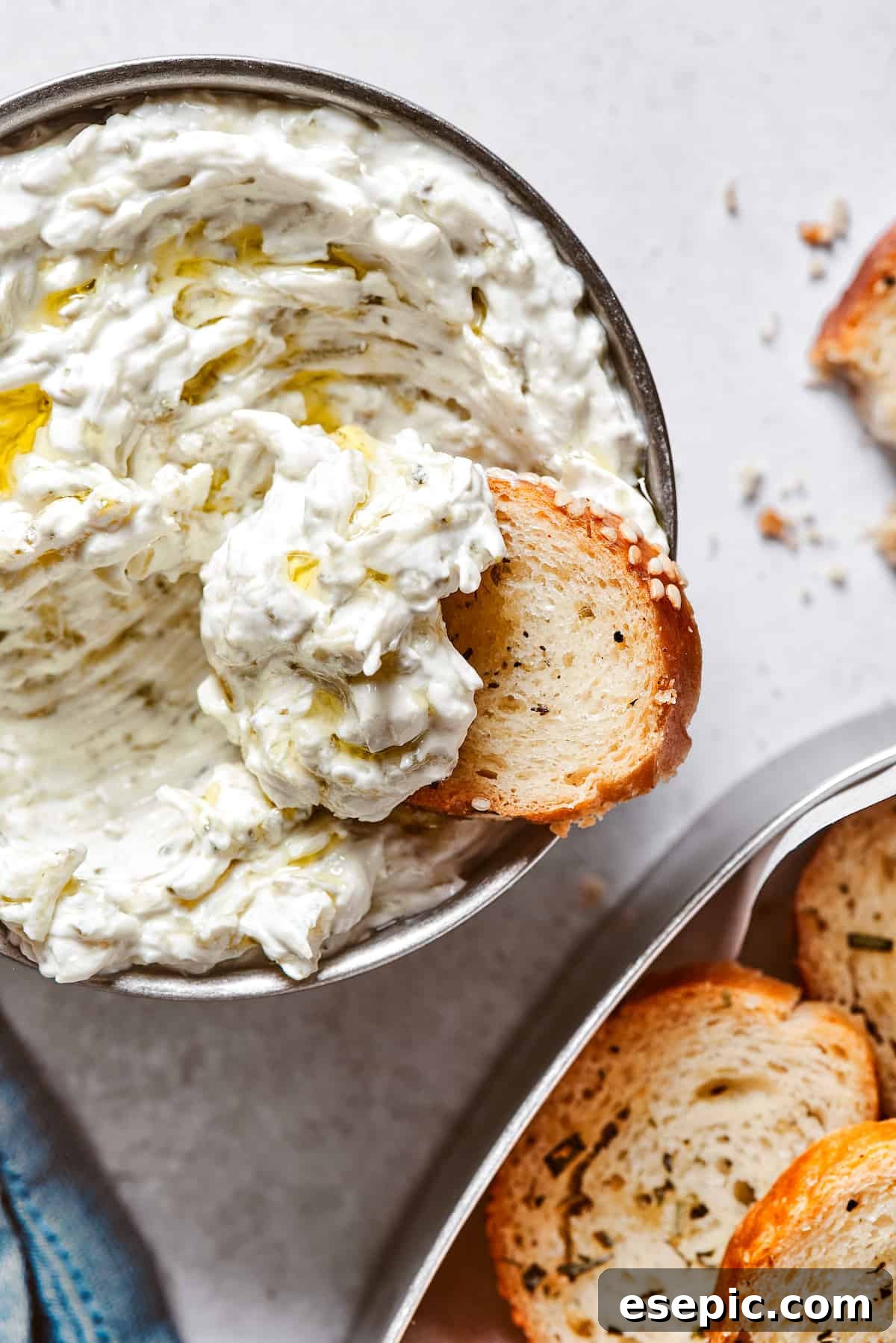 Scooping creamy dip out of a small bowl with a spoon, ready to be enjoyed with bagel chips.
