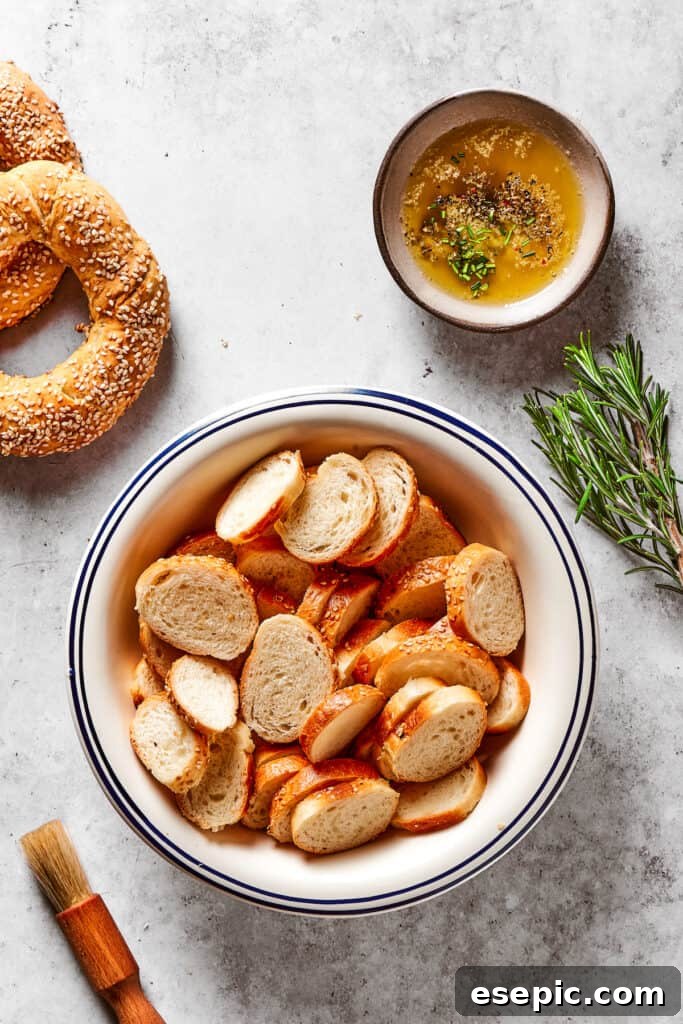 Homemade Bagel Chips: Buttery, crunchy, savory, and incredibly easy to make for a truly addictive snack experience! Sliced bagel rounds next to a dish of seasoned butter and a sprig of rosemary.