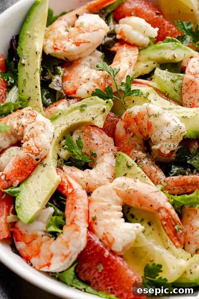 cooked shrimp, avocado slices, and salad greens tossed together in a white serving bowl