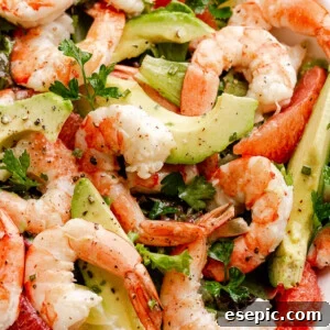 cooked shrimp, avocado slices, and salad greens tossed together in a white serving bowl