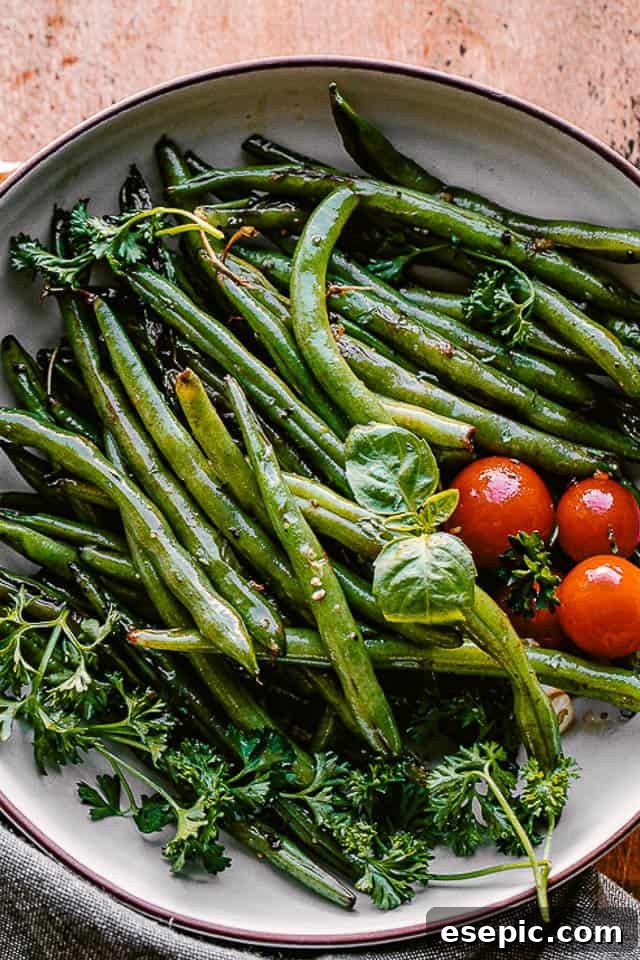 cooked green beans served in a bowl with fresh basil and cherry tomatoes, ready to be enjoyed