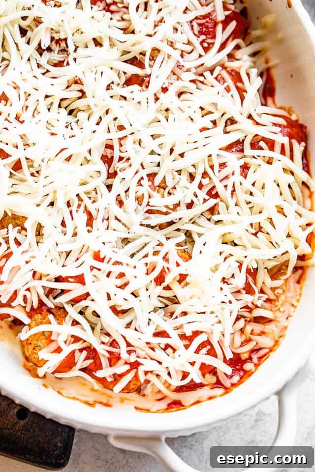 Cheesy baked meatball casserole with mini meatballs topped with your favorite marinara and loads of melty cheese! An easy dinner idea! A casserole dish filled with meatballs already covered in marinara sauce, now topped with a generous layer of shredded mozzarella cheese, glistening and ready for its final bake.