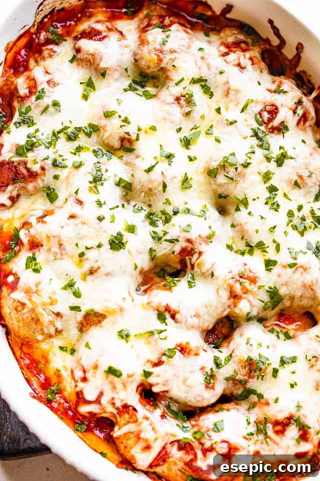Cheesy baked meatball casserole with mini meatballs topped with your favorite marinara and loads of melty cheese! An easy dinner idea! Close-up shot of a white baking dish filled with Cheesy Baked Meatball Casserole, showcasing the perfectly melted, bubbly mozzarella cheese over the savory marinara-covered meatballs, fresh out of the oven.