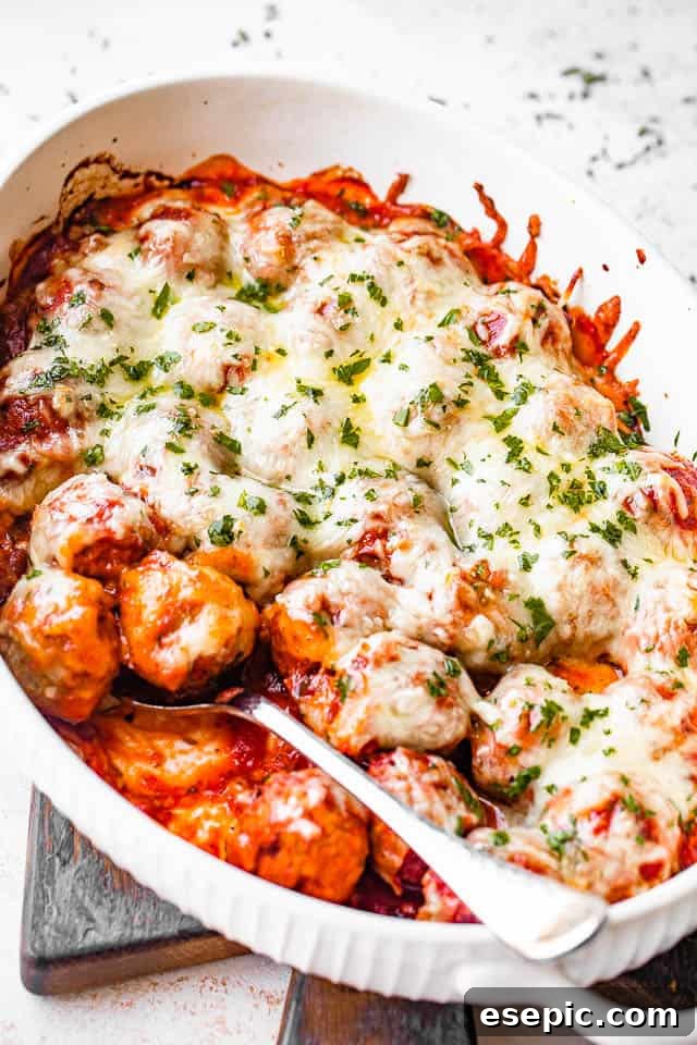 Cheesy baked meatball casserole with mini meatballs topped with your favorite marinara and loads of melty cheese! An easy dinner idea! A pristine white baking dish filled to the brim with Cheesy Baked Meatball Casserole, showcasing the rich marinara and a perfectly melted, golden-brown cheese topping, garnished with fresh parsley.