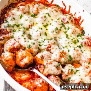 A beautiful white baking dish filled with golden-brown baked meatballs, covered in vibrant marinara sauce and a thick layer of perfectly melted mozzarella cheese.