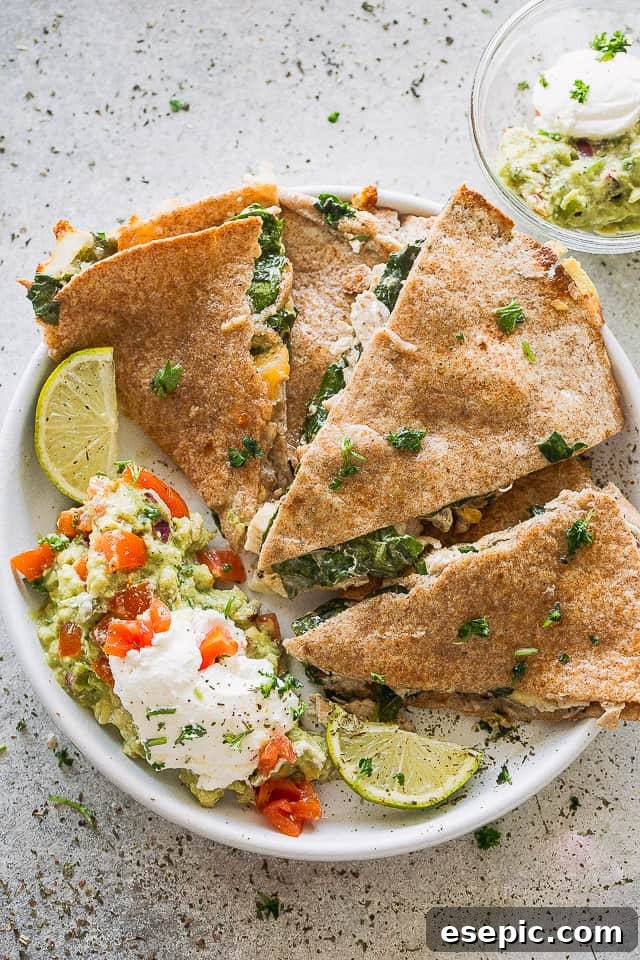 These baked chicken quesadillas are stuffed with fresh spinach, melted cheese and shredded chicken. It's 100% kid approved and oh so good! A plate of baked quesadillas served with dollops of sour cream and guacamole.