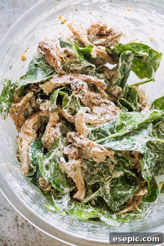 These baked chicken quesadillas are stuffed with fresh spinach, melted cheese and shredded chicken. It's 100% kid approved and oh so good! Mixing the quesadilla ingredients in a bowl, showing shredded chicken, spinach, and spices.