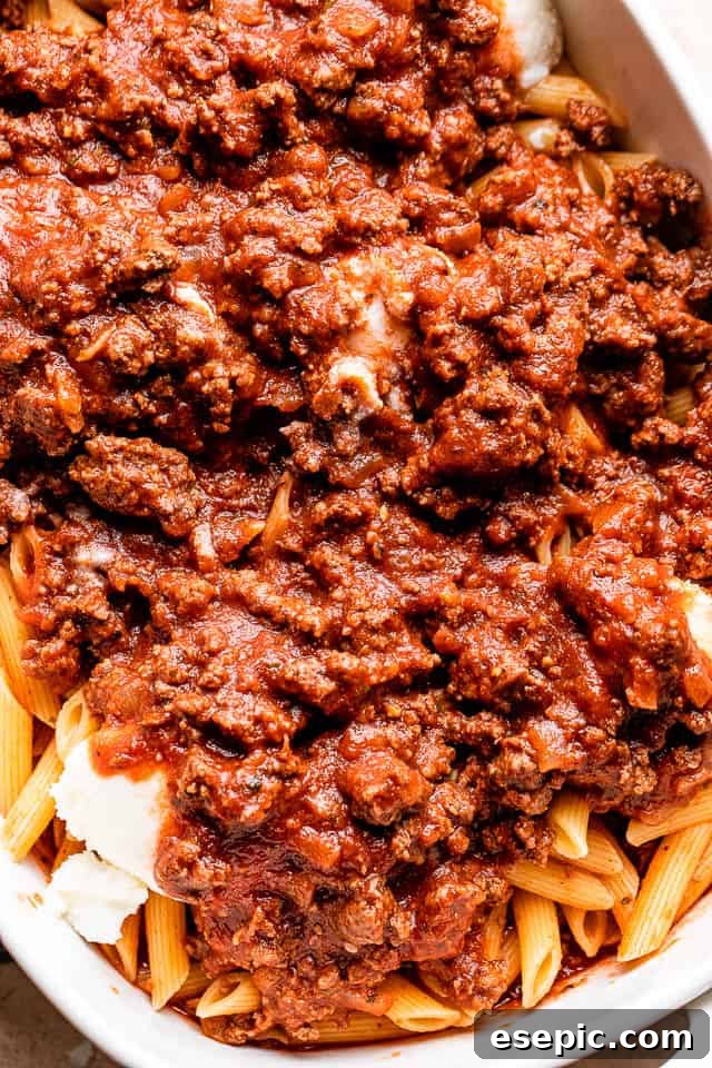 The Ultimate Cheesy Baked Ziti 4 A large pot of cooked ziti pasta being mixed with a generous amount of rich ground beef tomato sauce.