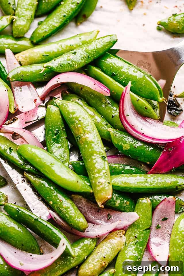 scooping up roasted snap peas from a baking sheet