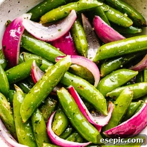 roasted sugar snap peas with red onions served in a cream bowl