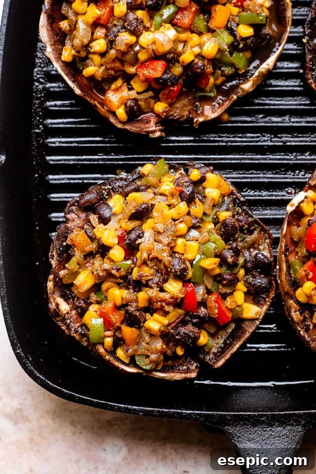 Two portobello mushrooms, beautifully stuffed with black beans and corn, glistening with melted cheese, sizzling on an outdoor grill rack.