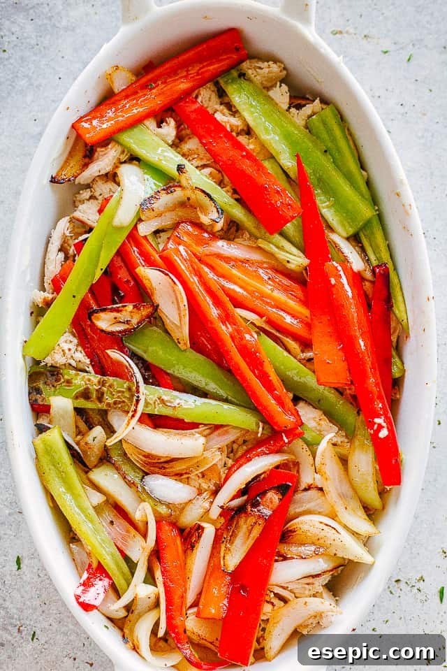 Bell pepper strips arranged over shredded chicken in an oval baking dish before mixing.
