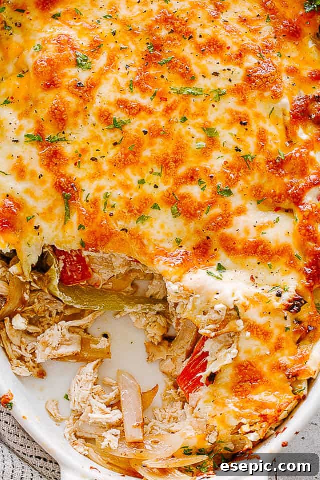 close up view of a chicken fajita casserole in a white oval baking dish, showing melted cheese and colorful vegetables.
