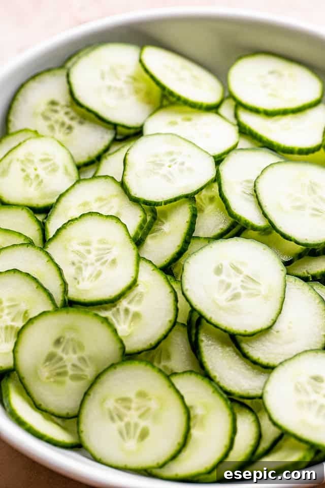 Freshly sliced English cucumbers arranged in a white bowl, prepped and ready for salad preparation.