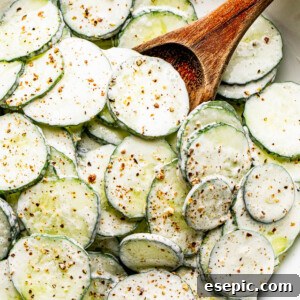 A vibrant bowl of cucumber salad coated in a creamy sour cream dressing, lightly seasoned with cracked black pepper, presented for a healthy meal.