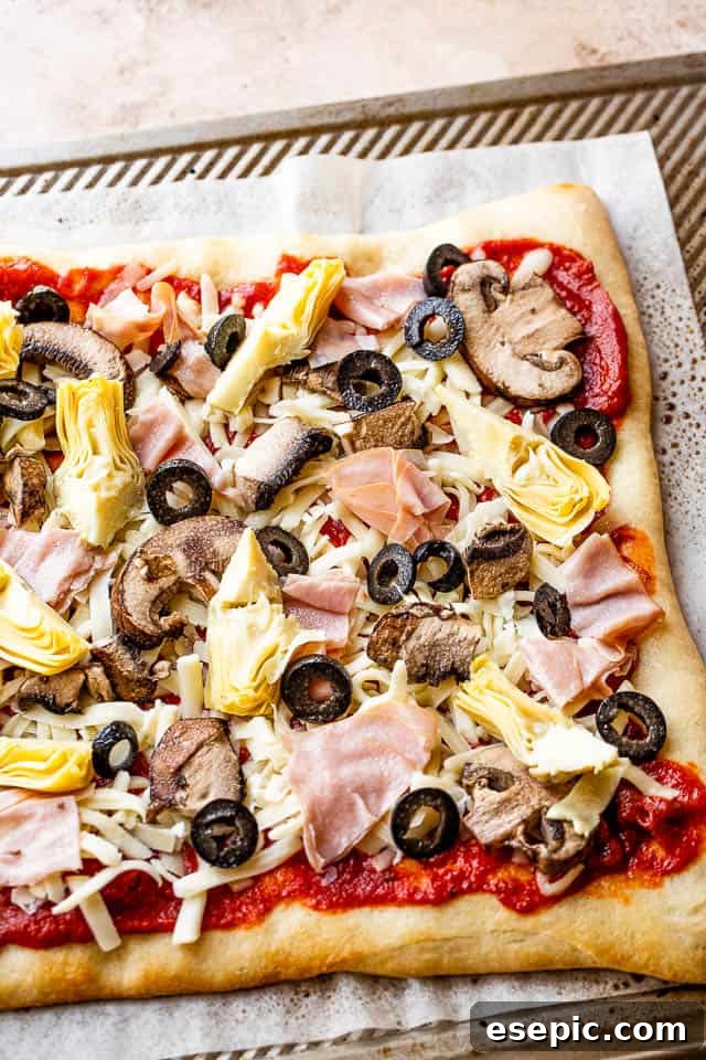 A delectable assembly of tomato sauce, shredded cheese, quartered artichoke hearts, sliced olives, and chopped ham meticulously arranged on a pizza crust, perfectly prepped for grilling.