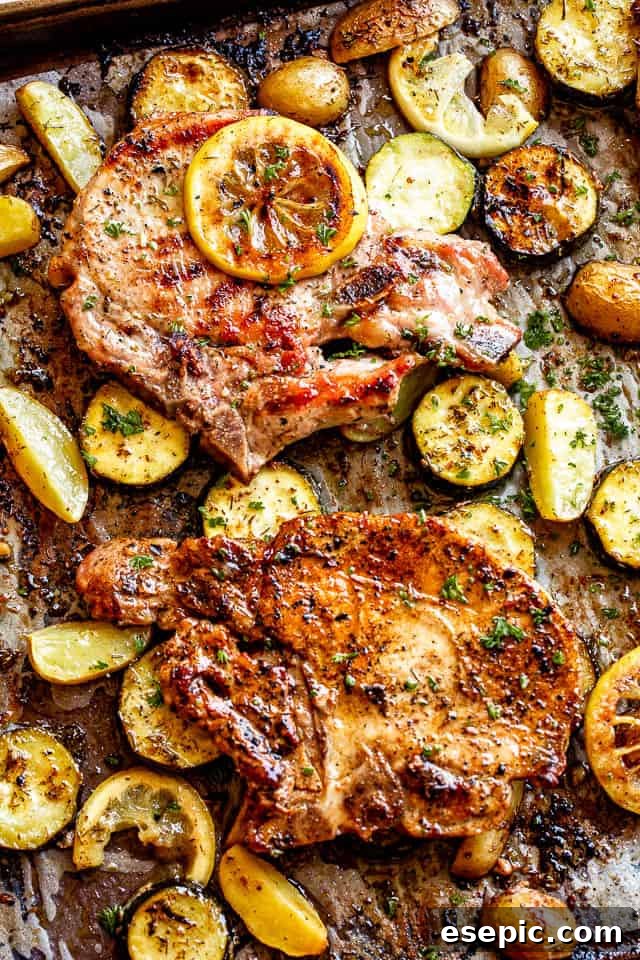 Sheet pan with baked pork chops nestled among slices of colorful squash and lemon wedges