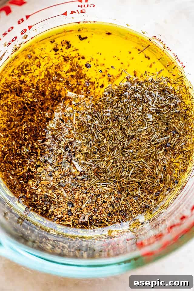 Glass measuring cup filled with a vibrant lemon garlic marinade infused with dried herbs