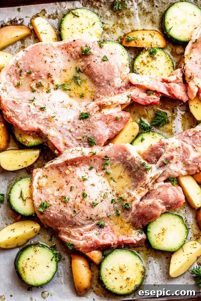 Baking sheet prepared with raw pork chops placed over seasoned squash and potato slices
