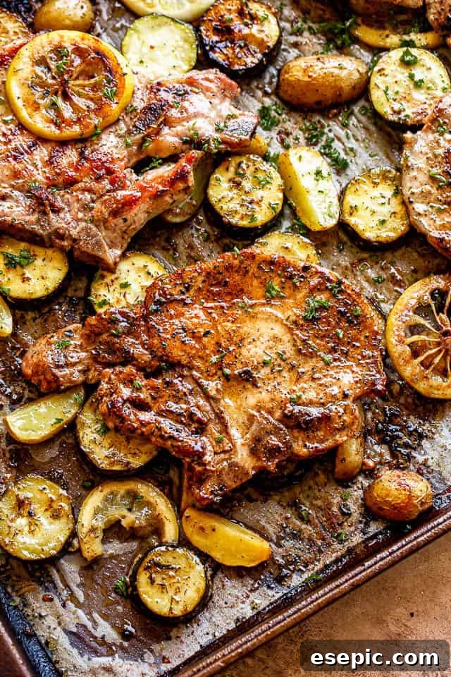 Another view of the baked pork chops on a sheet pan with squash and lemon slices, ready to serve
