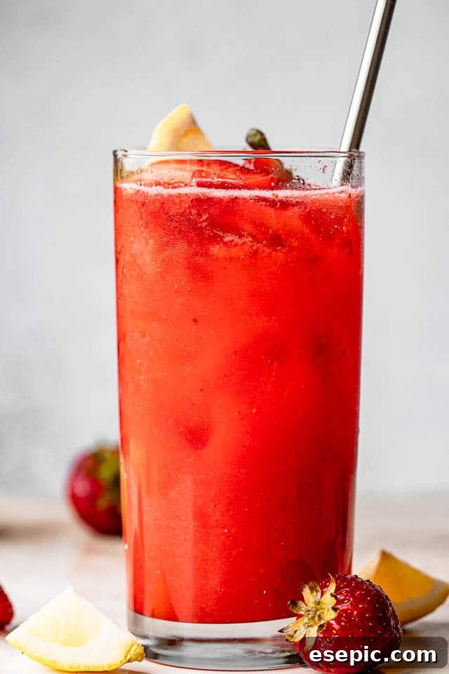 Close-up of a tall glass filled with vibrant Strawberry Lemonade Sangria, showing its refreshing color.