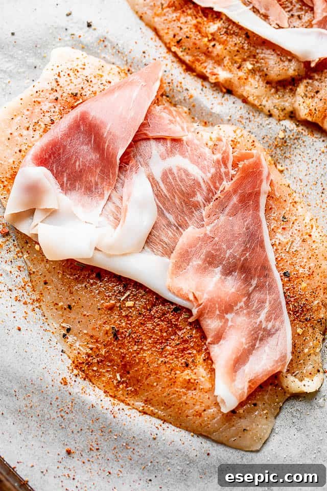 Slice of prosciutto laid over a raw chicken breast, ready for filling