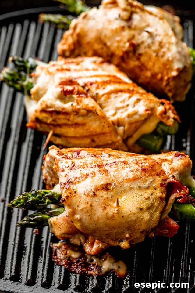 Three chicken roll ups cooking on a grill pan, stuffed with asparagus, prosciutto, and cheese