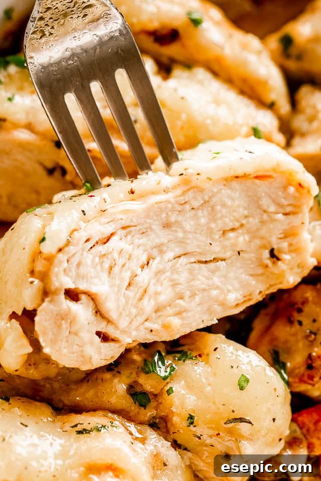 Close-up view of a fork piercing a tender slice of baked Caesar chicken breast, showcasing its juicy texture and rich cheesy coating.