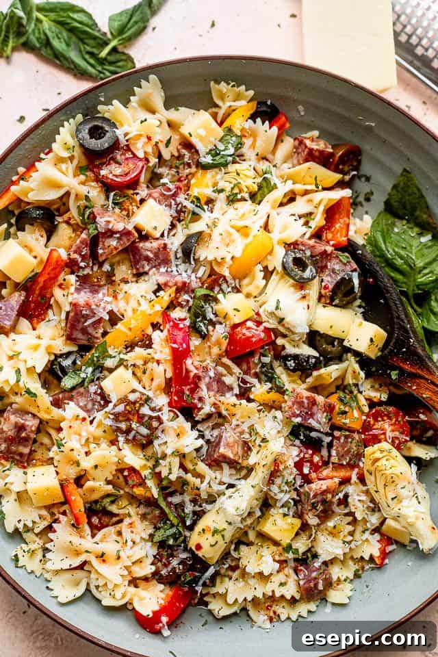 Italian Deli Pasta Salad 5 top view shot of a wooden spoon in a bowl filled with pasta, cheese cubes, salami cubes, tomatoes, and olives