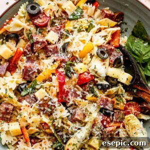 top view shot of a wooden spoon in a bowl filled with pasta, cheese cubes, salami cubes, tomatoes, and olives
