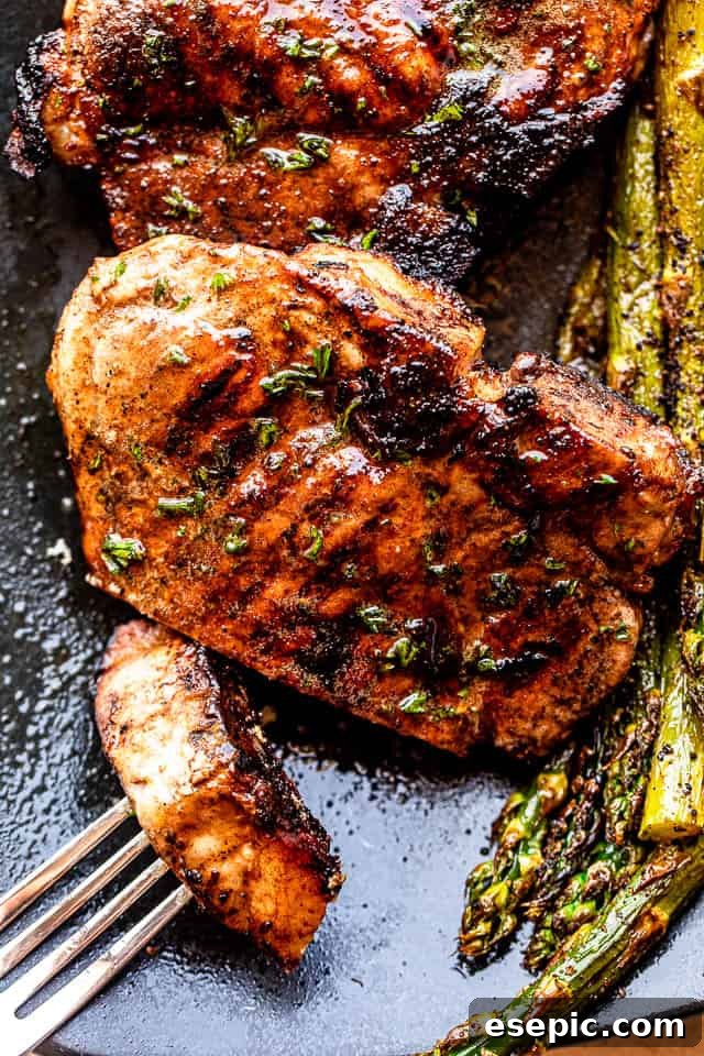 Serving of juicy grilled pork chops on a black plate with fresh asparagus