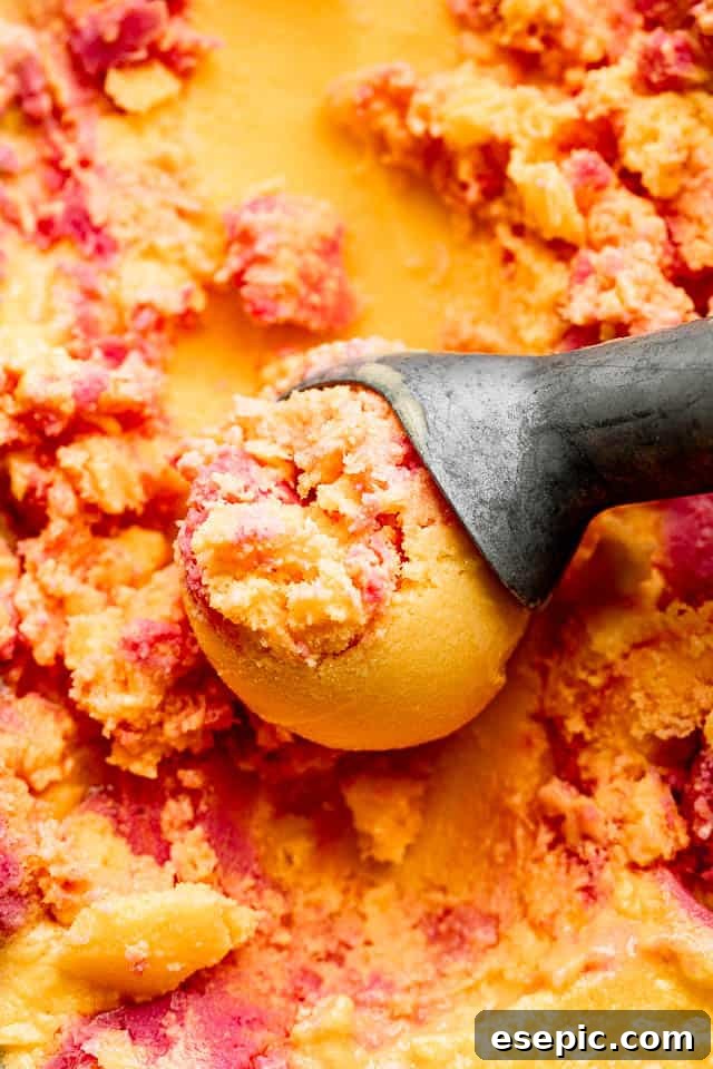Close-up shot of creamy mango strawberry frozen yogurt in an ice cream scoop, showcasing its vibrant layers