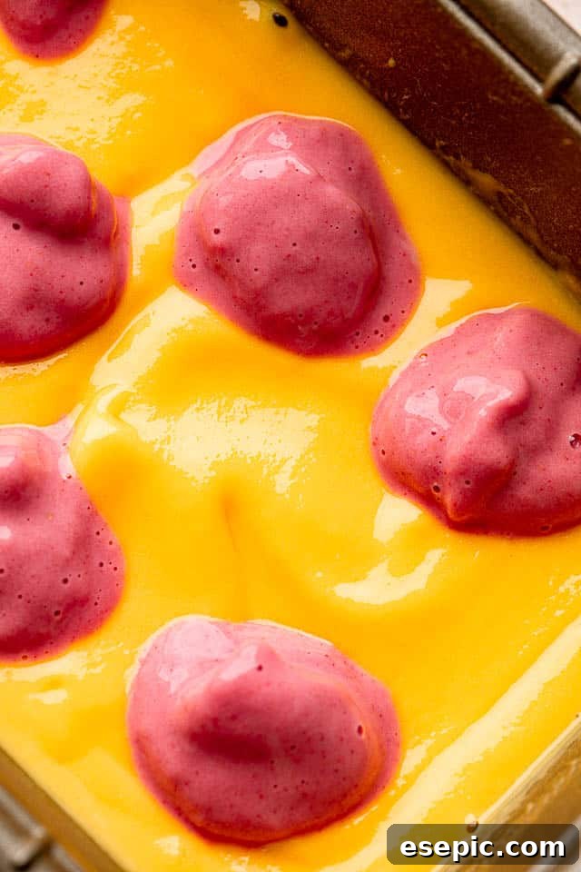 Close-up shot of a blended mango mixture in a pan, topped with dollops of a vibrant blended strawberry mixture
