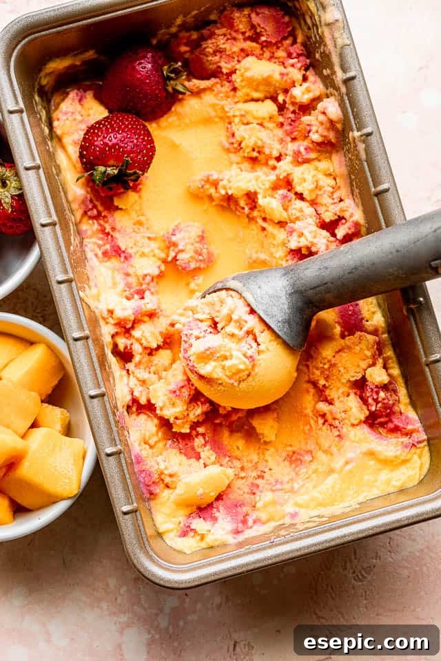 Top shot of mango strawberry frozen yogurt in a loaf pan with an ice cream scooper, showing the marbled effect