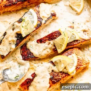 white pan with four salmon fillets topped with lemon slices and cream sauce, captured from an overhead angle.