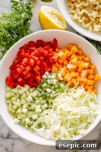 Bowls of macaroni salad ingredients laid out, including cooked pasta, chopped vegetables, and dressing components, ready for mixing.