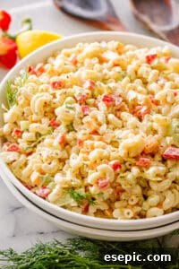 A large mixing bowl containing cooked elbow macaroni, freshly chopped vegetables, and cubed cheddar cheese, tossed together before adding the dressing.